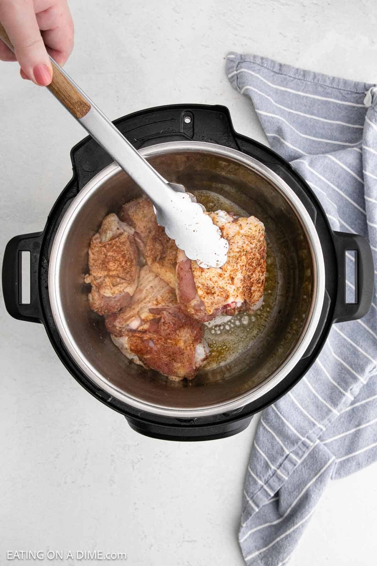 Placing the chicken thighs with tongs in the instant pot with the melted butter