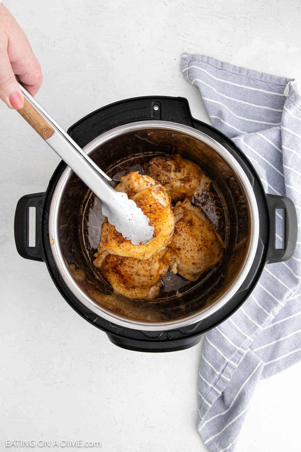Removing the seared chicken thighs from the instant pot with tongs