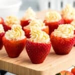 Cheesecake Stuffed Strawberries with the tops cut off and hollowed out, filled with a creamy cheesecake mixture, are beautifully arranged on a wooden board.