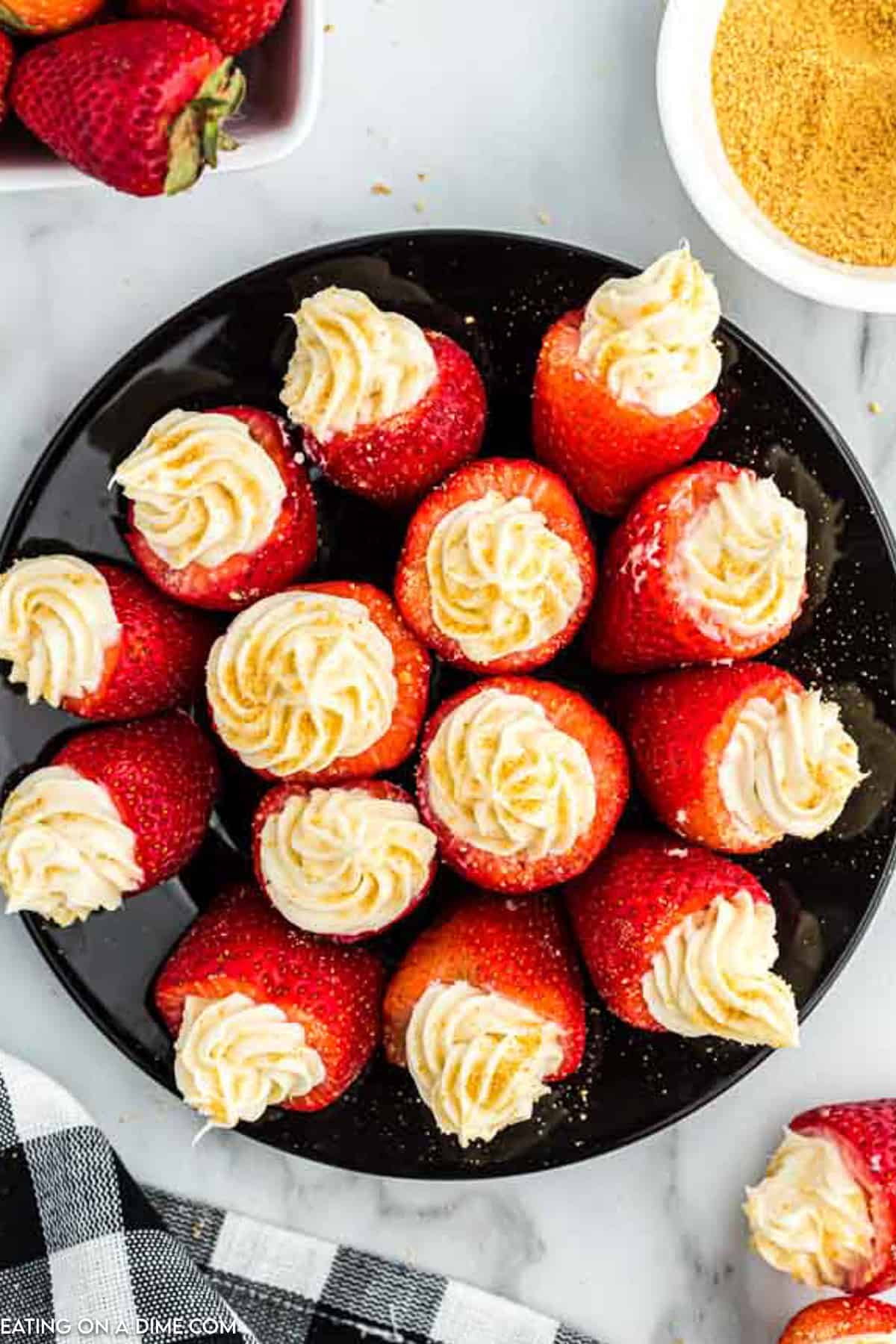 Cheesecake Stuffed Strawberries placed on a black plate topped with crushed graham crackers