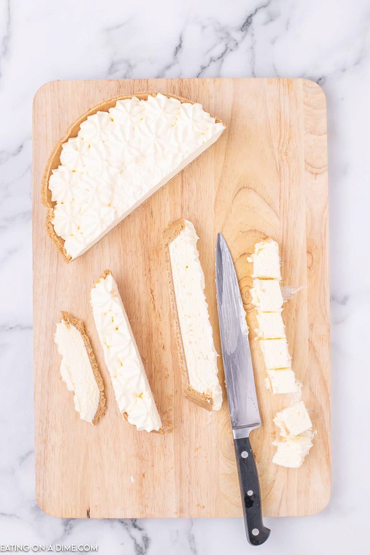 Slicing frozen cheesecake on a cutting board with a sharp knife