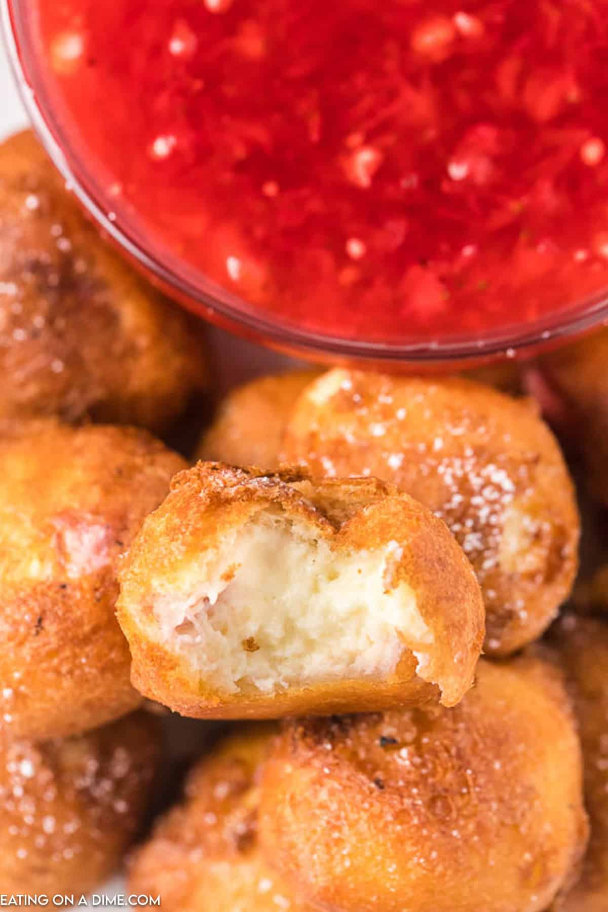 Deep Fried Cheesecake Bites stacked on a platter with a bowl of strawberry sauce