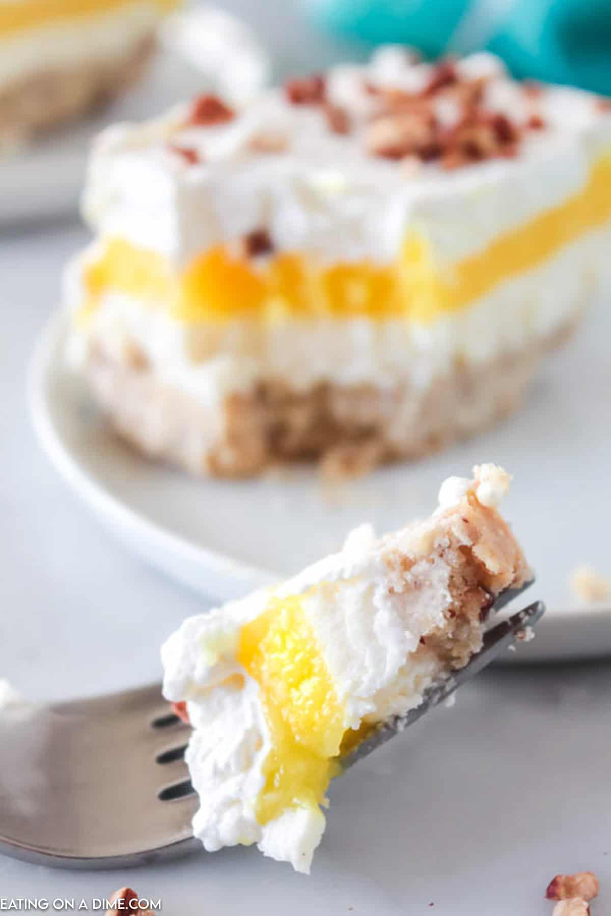 A bite of lemon lush on a fork with a slice of lemon lush dessert in the background on a plate
