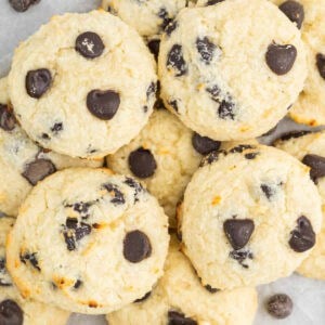 A close-up of several round cottage cheese cookies, golden on the edges and studded with dark chocolate chips, arranged in an overlapping pile—a delicious twist on classic cottage cheese desserts.