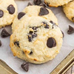 Close-up of golden Cottage cheese cookies on a baking sheet lined with parchment paper, with a few chocolate chips scattered around. These cookies are slightly crisp on the edges—a delicious twist on classic cottage cheese recipes.
