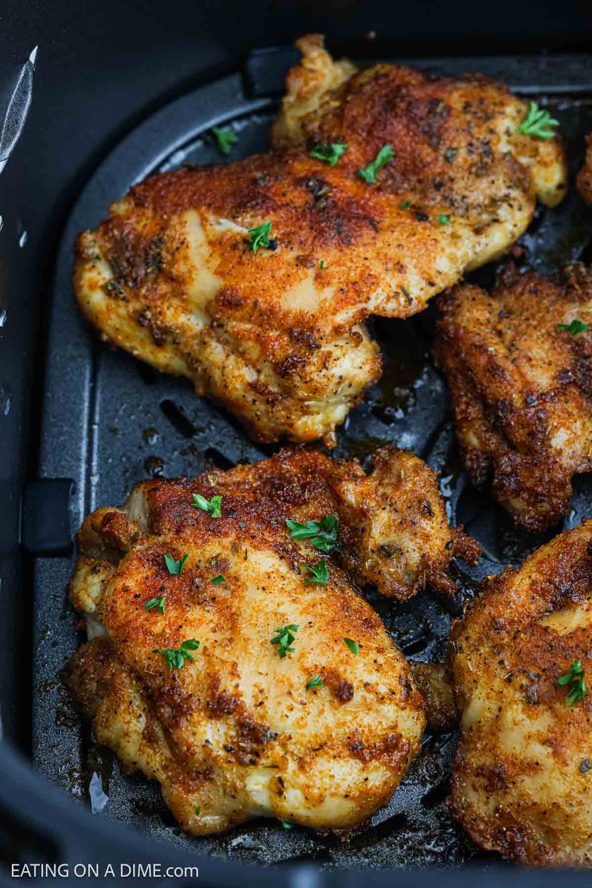 Seasoned boneless chicken thighs with a golden-brown, crispy crust, garnished with chopped herbs, arranged neatly in an air fryer basket.