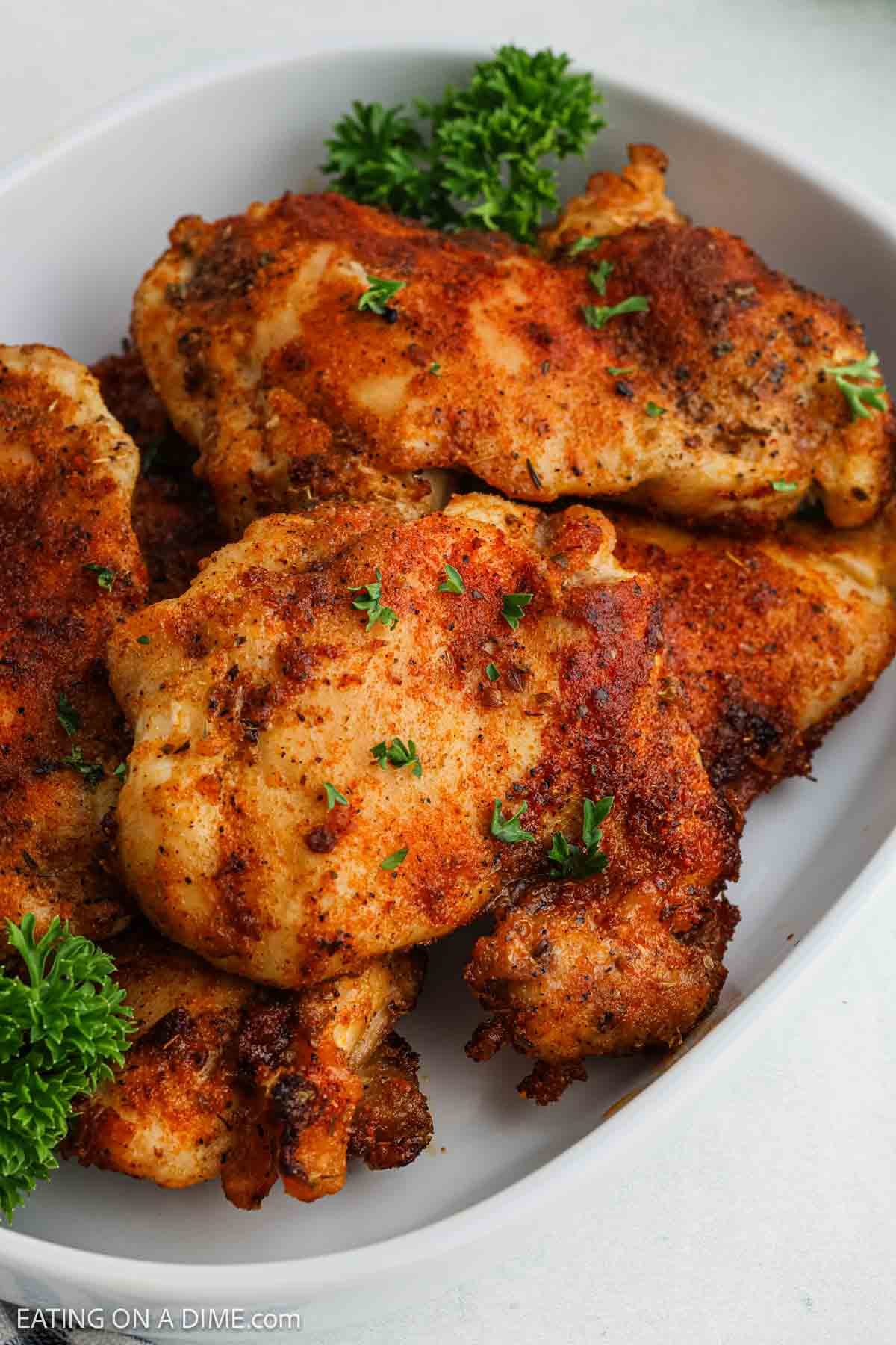 A plate of air fryer chicken thighs garnished with fresh parsley, served on a white dish. The boneless chicken thighs have a golden-brown, crispy coating and are perfectly seasoned and grilled.