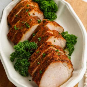Air Fryer Pork Tenderloin sliced and seasoned, arranged neatly on a white oval platter and garnished with fresh parsley.