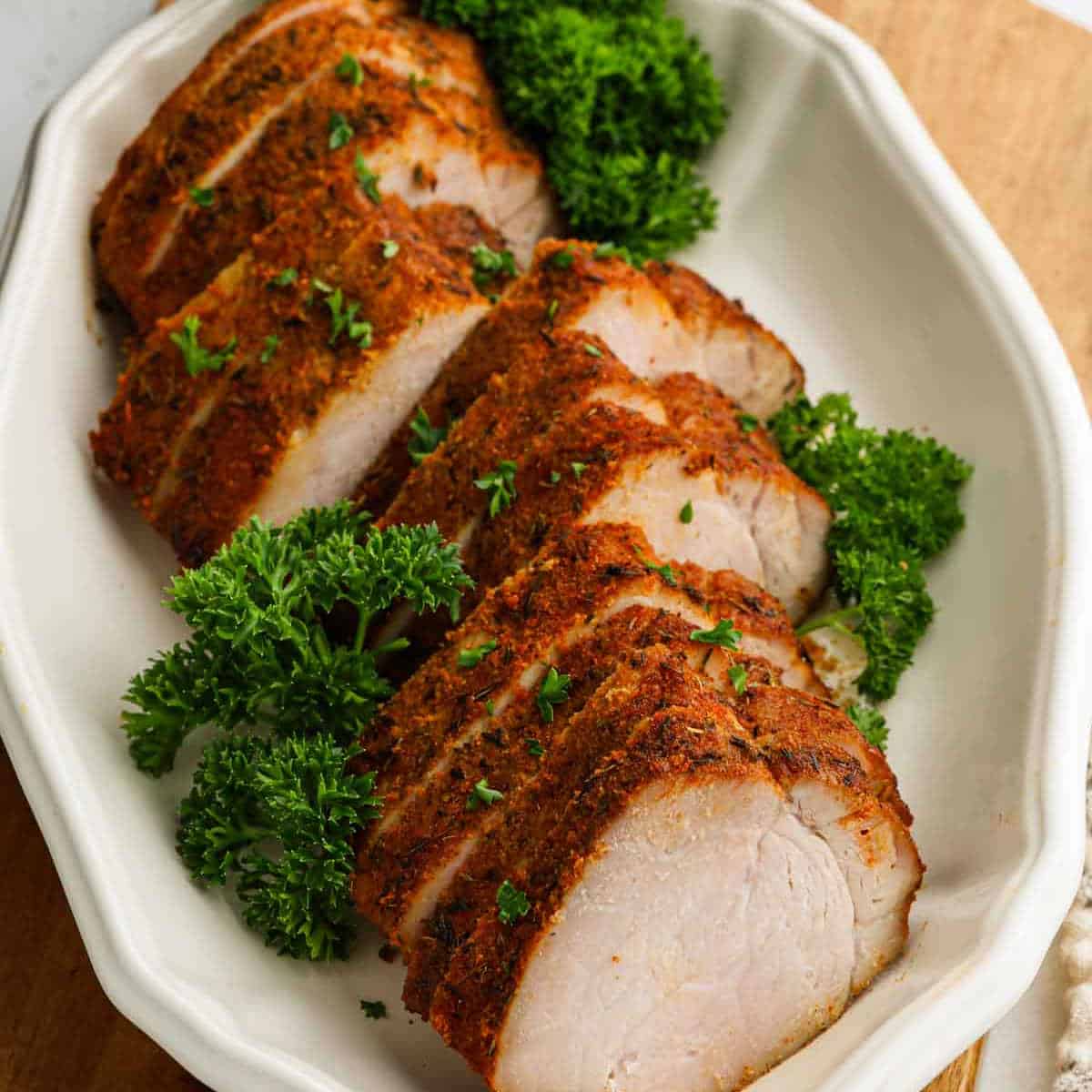 Air Fryer Pork Tenderloin sliced and seasoned, arranged neatly on a white oval platter and garnished with fresh parsley.