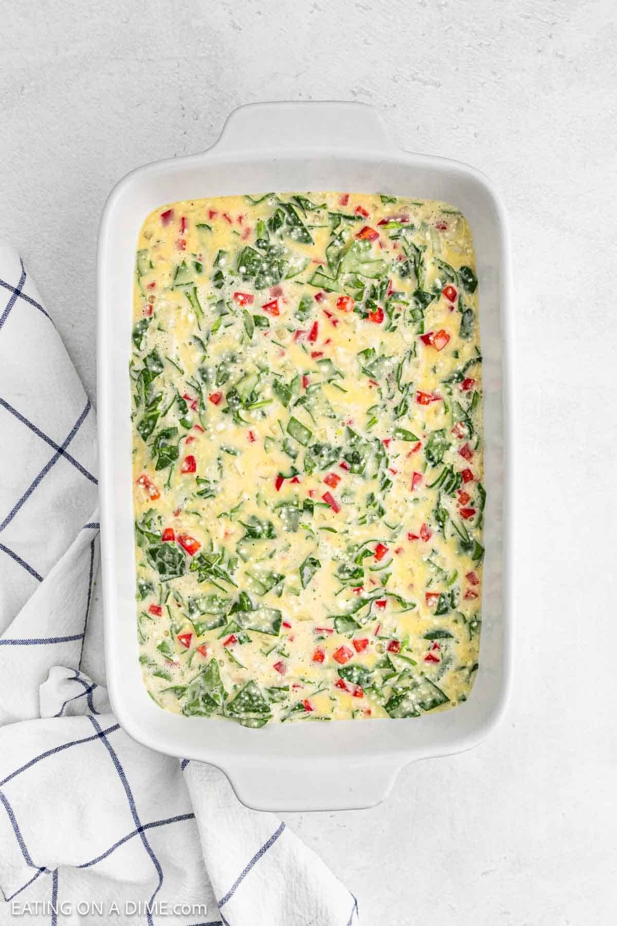 Egg casserole with the chopped spinach, red bell pepper poured into the baking dish