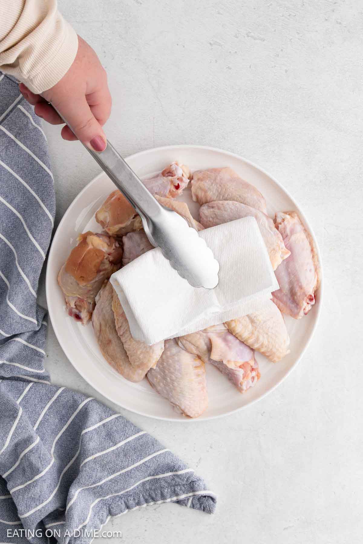 Drying the chicken wings with a paper towel with tongs on a plate