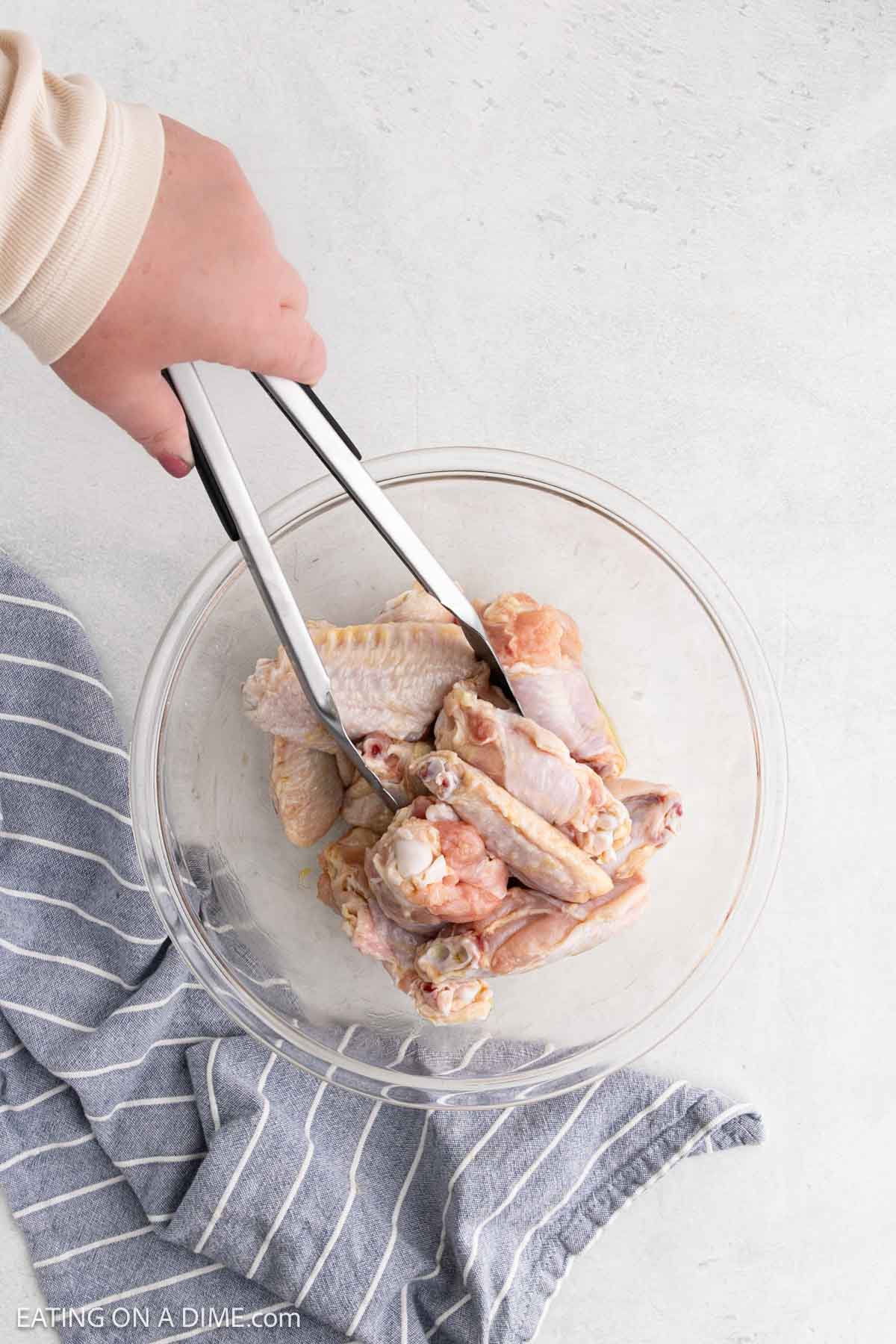 Uncooked chicken wings in a bowl with tongs tossing them
