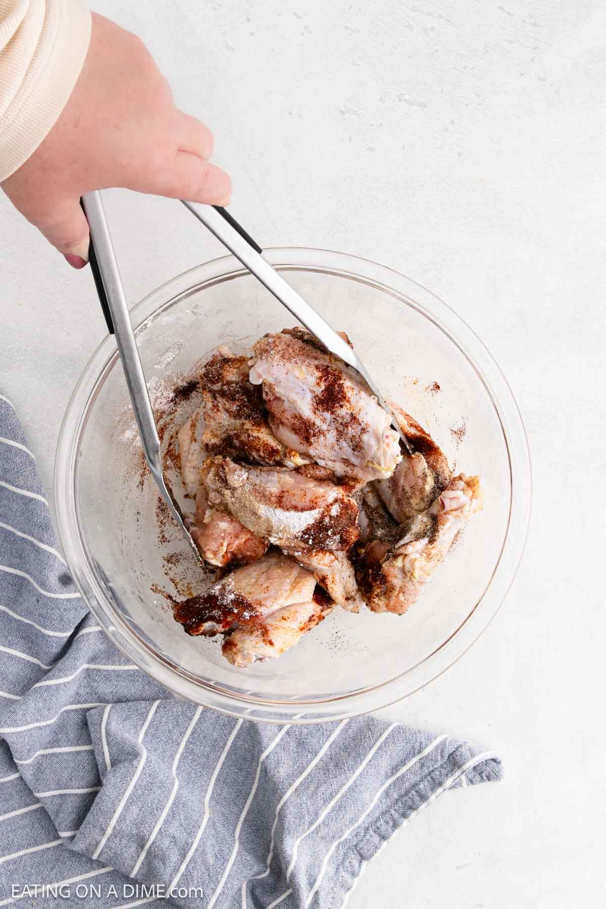 Adding the seasoning to the uncooked chicken wings in a bowl with tongs tossing them