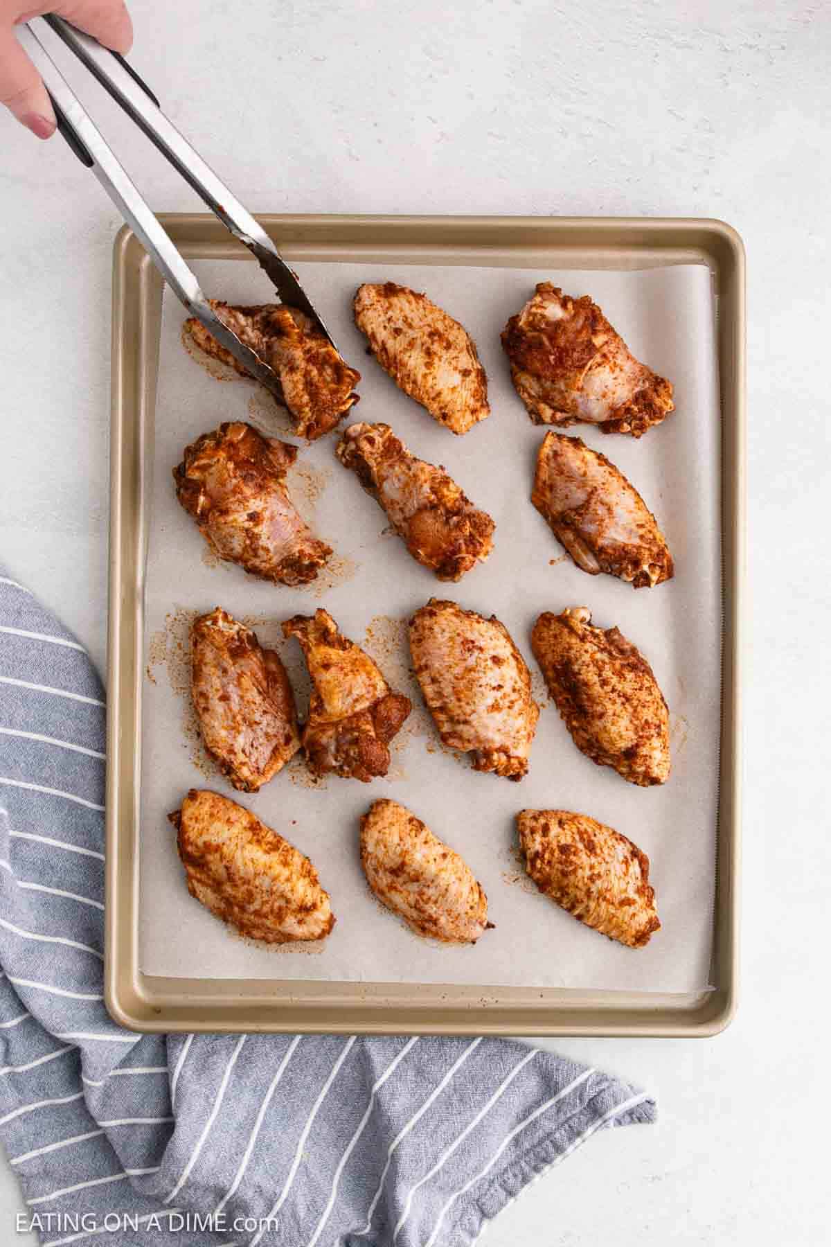 Placing the seasoned raw chicken wings on a baking sheet lined with parchment paper