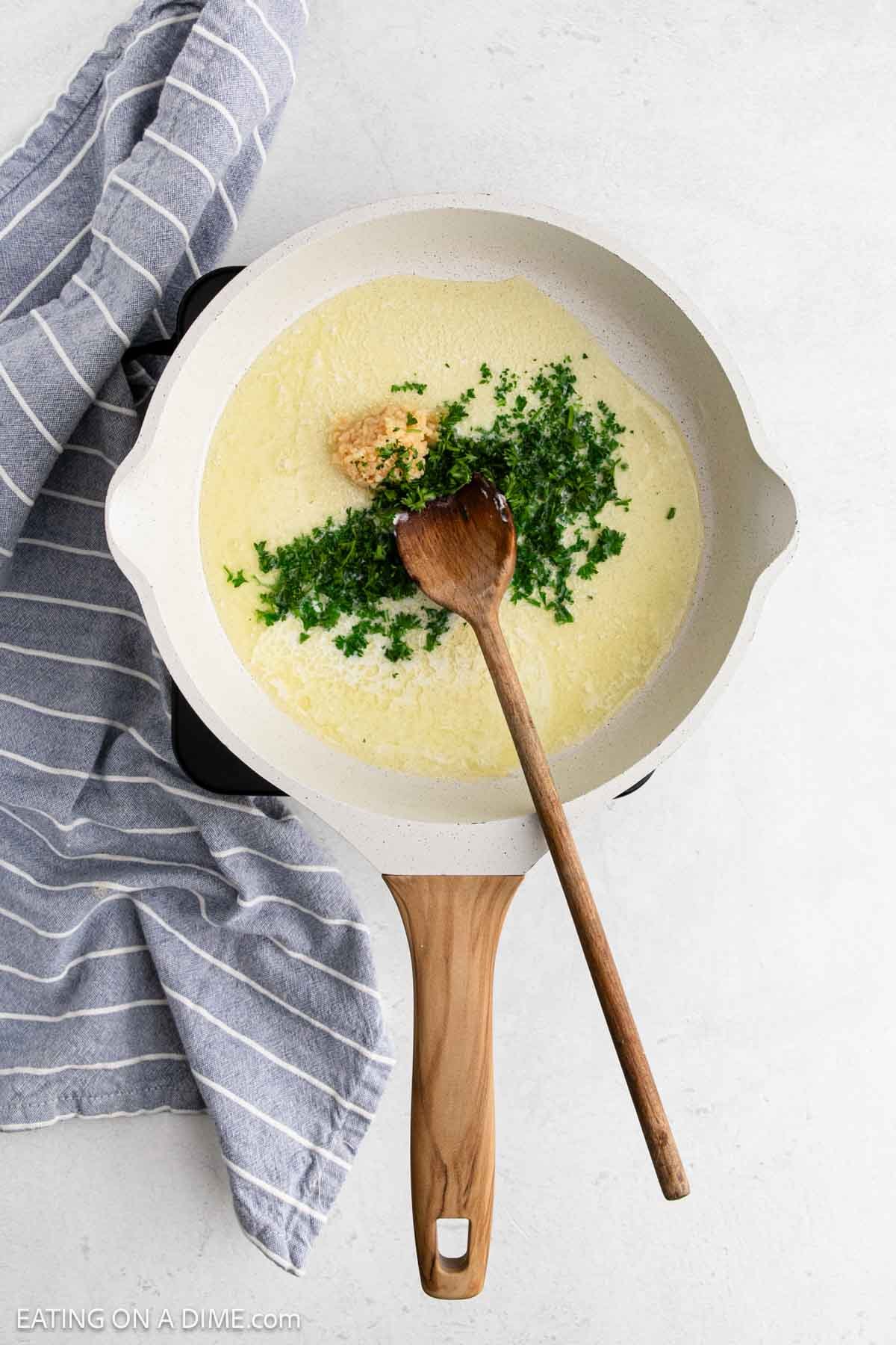 Adding in the chopped parsley and minced garlic with melted butter in a skillet with a wooden spoon