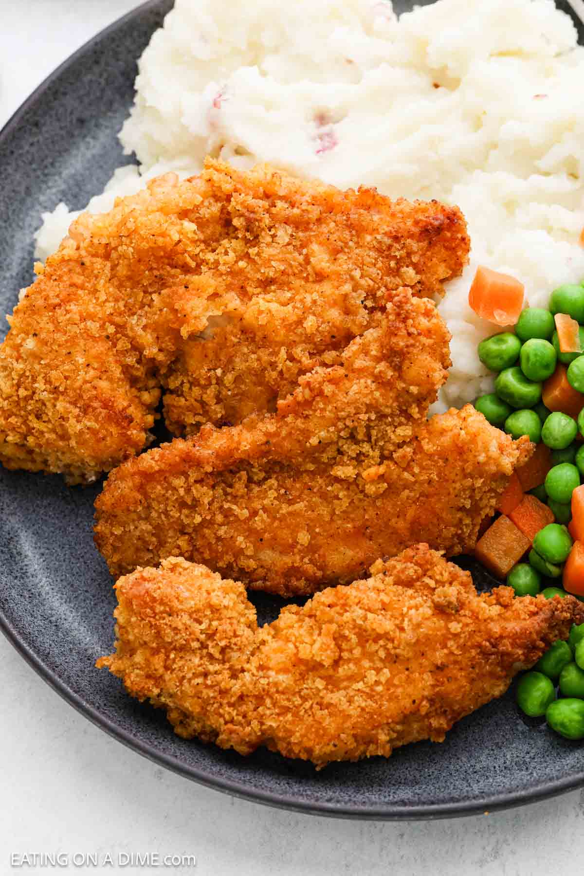 Oven Fried Chicken Tenders on a plate with mashed potatoes and a peas and carrots mixture