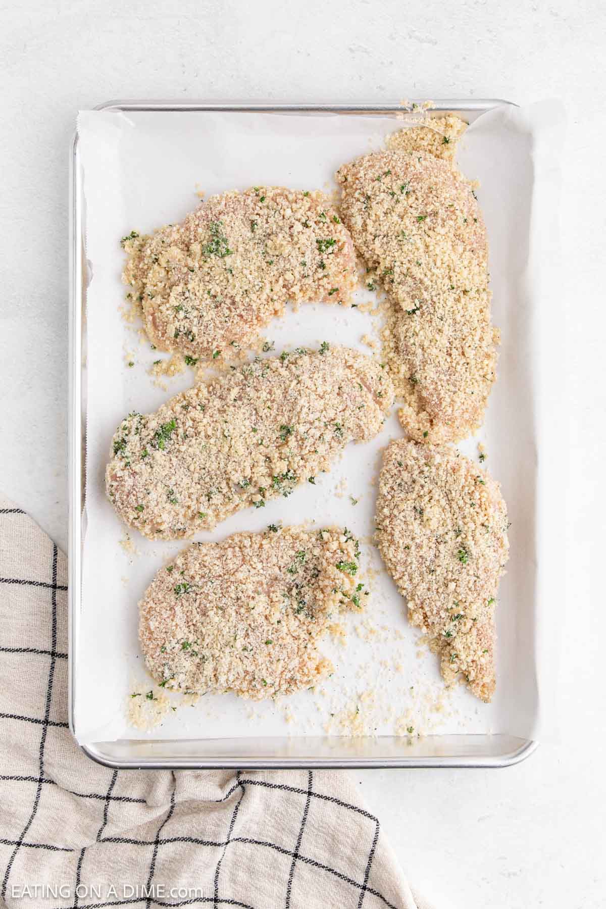 Chicken breast coated with the parmesan breadcrumb mixture on a baking sheet lined with parchment paper