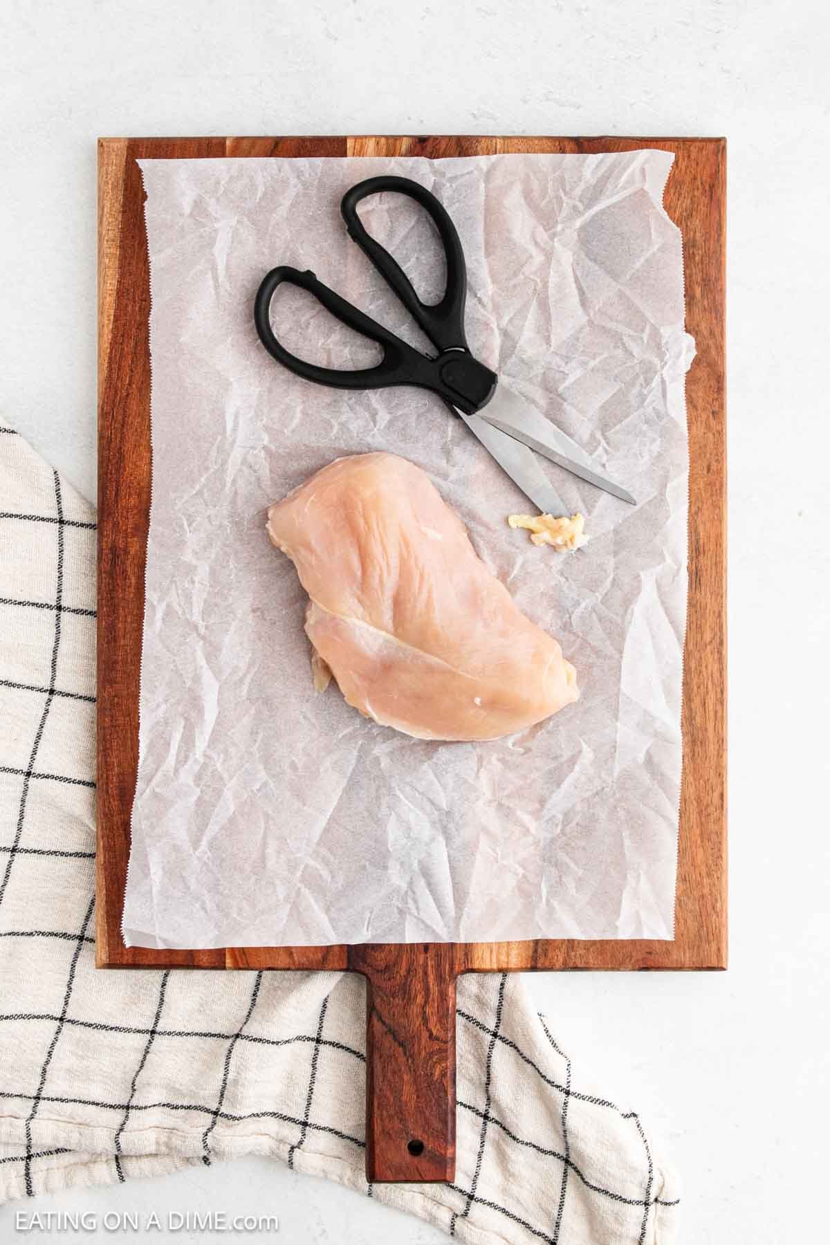 Cutting chicken breast on parchment paper covered wooden cutting board with kitchen spears