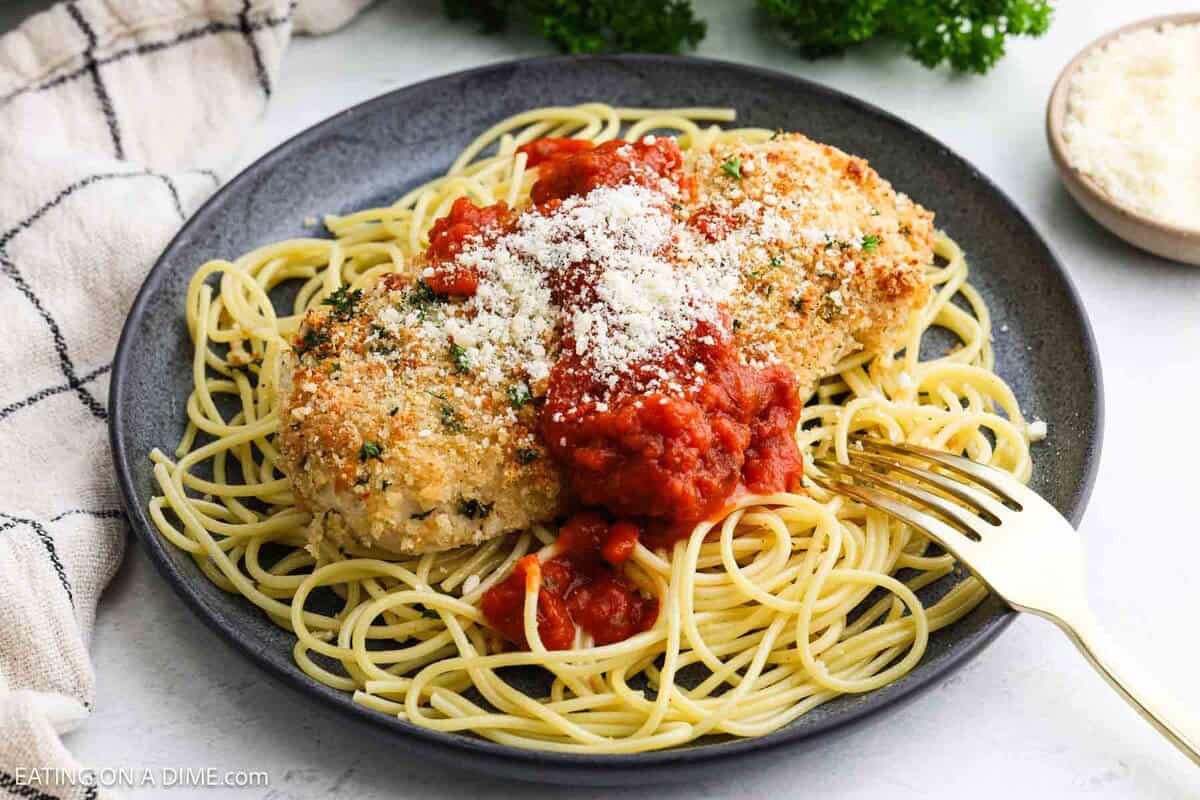 Parmesan Crusted Chicken breast on a plate over spaghetti noodles topped with sauce and parmesan cheese