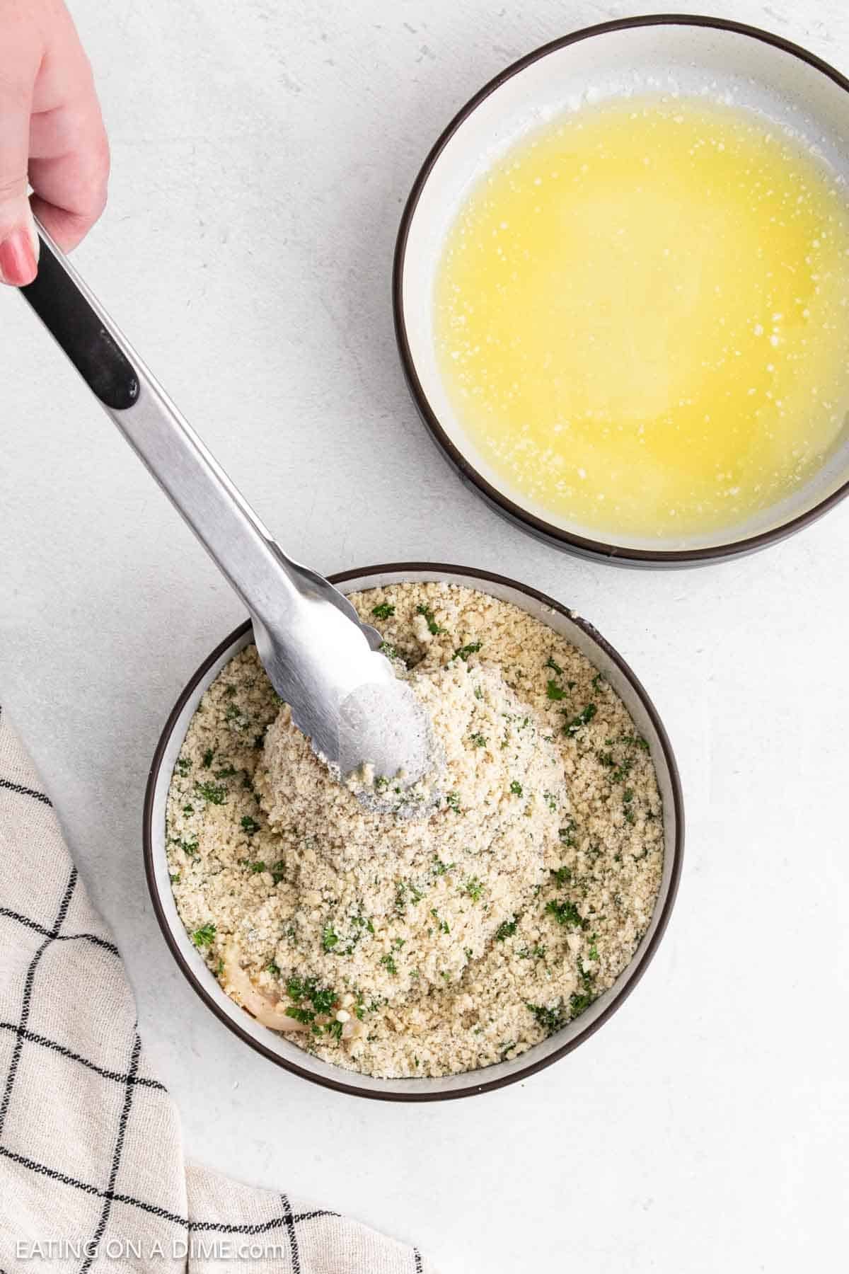 Placing the chicken breast in the parmesan mixture in a bowl with tongs with a bowl of melted butter on the side