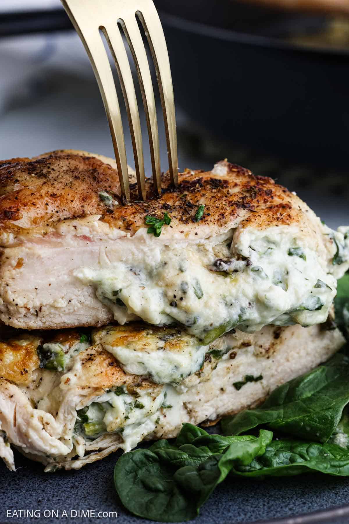 A close-up of a fork cutting into a Spinach Stuffed Chicken Breast, filled with a creamy spinach and cheese mixture, served on a plate with fresh spinach leaves.