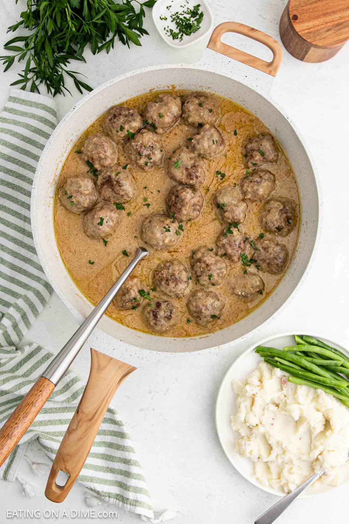 Swedish Meatballs in a large skillet with creamy gravy with a side of mashed potatoes and green beans on a plate