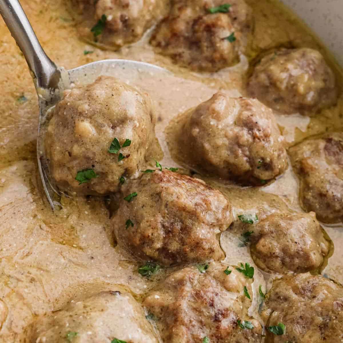 Swedish Meatballs in a pan of creamy gravy with a serving on a silver spoon