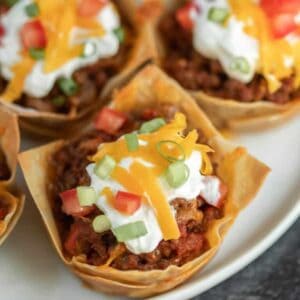 A close-up of taco cups made with crispy wonton wrappers, filled with seasoned ground beef, diced tomatoes, sour cream, cheddar cheese, and green onions—perfect for spicing up your Meal Plan 53 or adding variety to any meal plan.