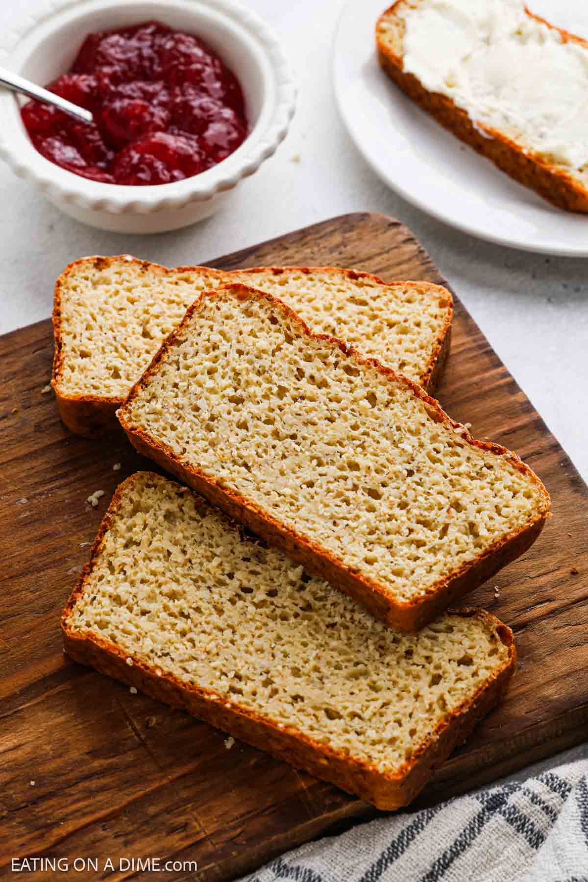 Sliced cottage cheese bread on a cutting board with a bowl of jam and a slice of bread topped with butter on a plate