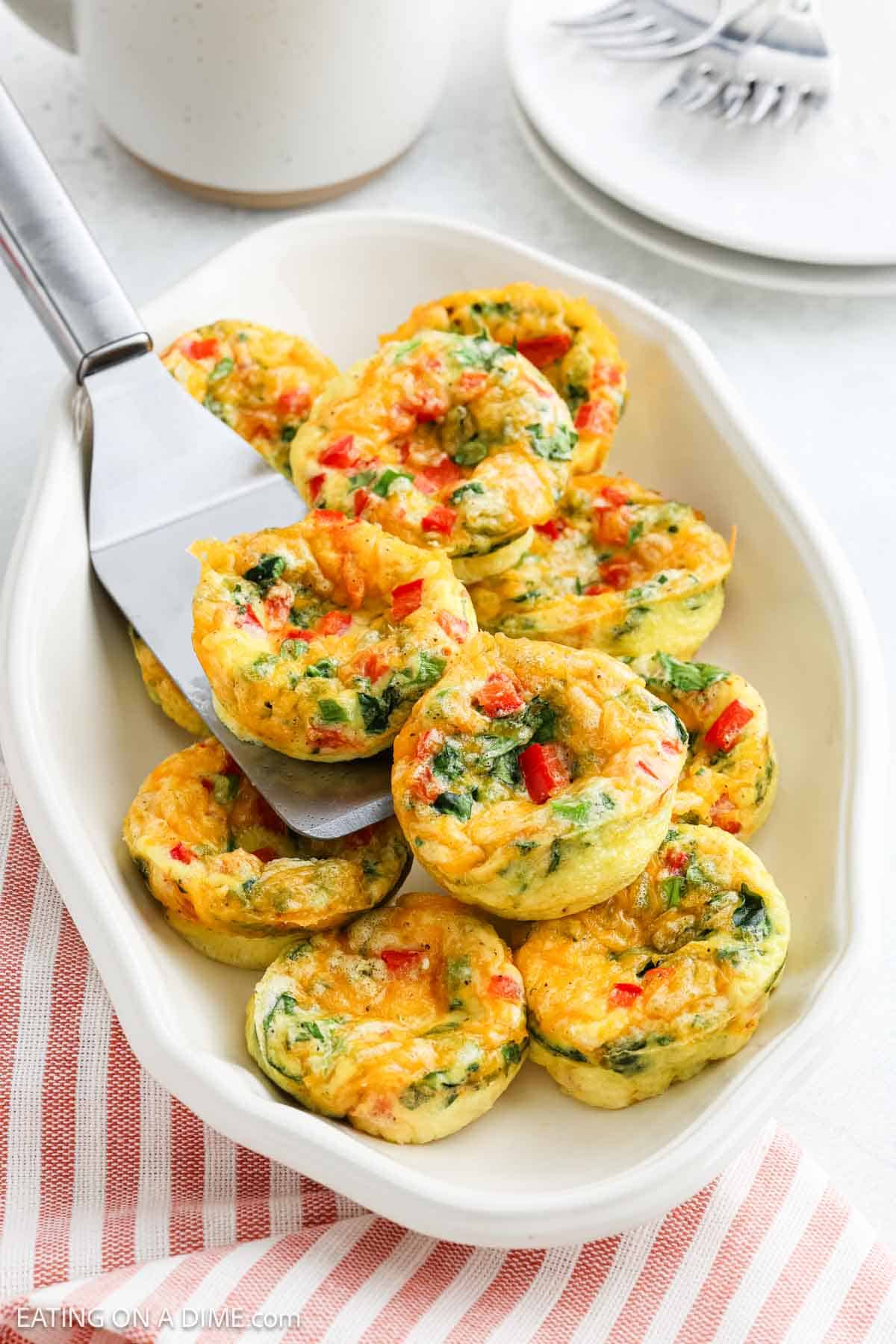 Cottage Cheese Egg Bites stacked on a white platter with a serving spatula