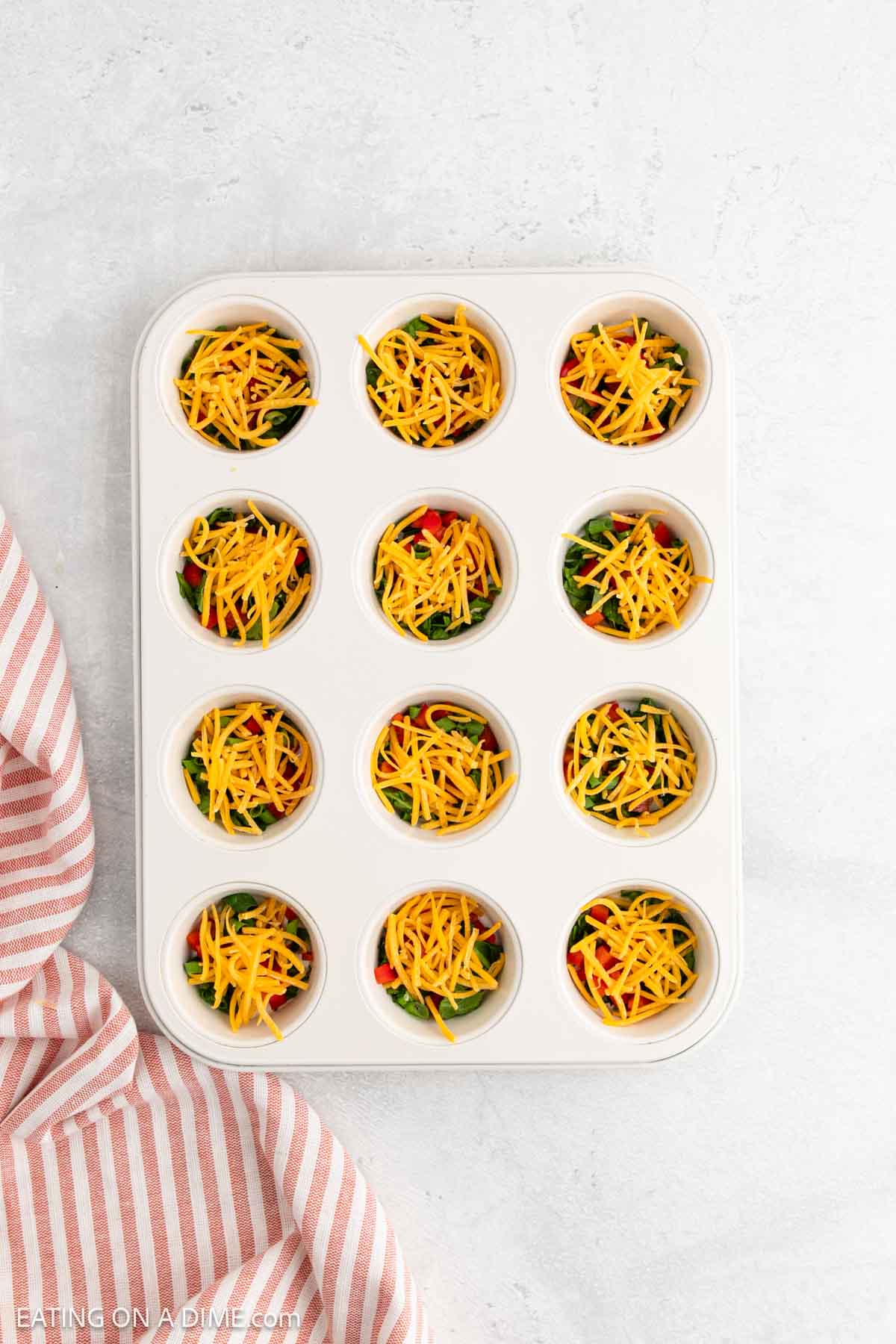Shredded cheese topped with chopped veggies in a muffin tin