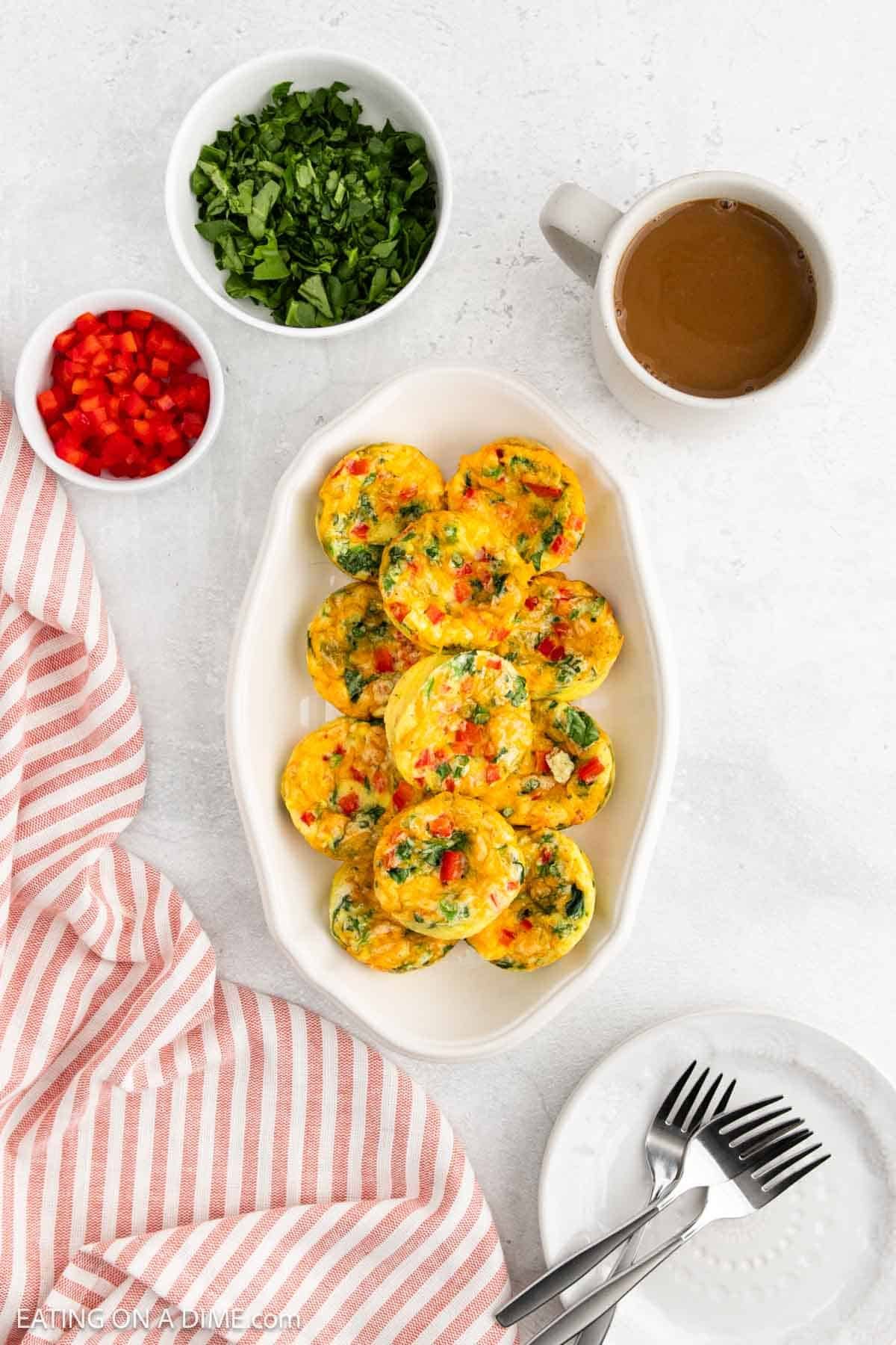 Cottage Cheese Egg Bites on a white platter with a bowl of chopped bell pepper and shredded spinach with a cup of coffee on the side