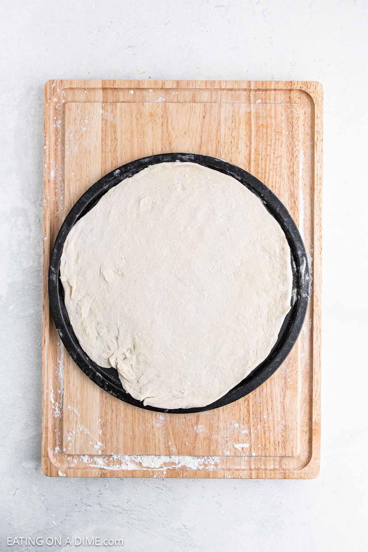 A round pizza pan with healthy pizza crust sits on a wooden cutting board against a light background, ready to be topped and baked.