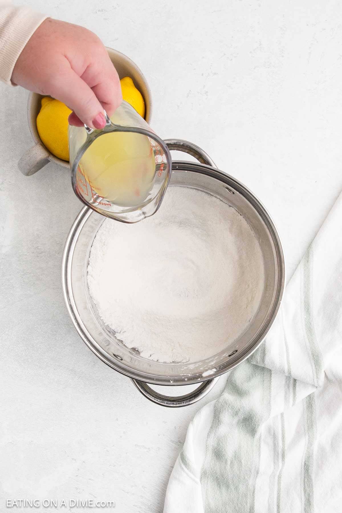 Sugar, cornstarch and salt mixed together in a large pot with a clear bowl pouring in the lemon juice into the sugar mixture