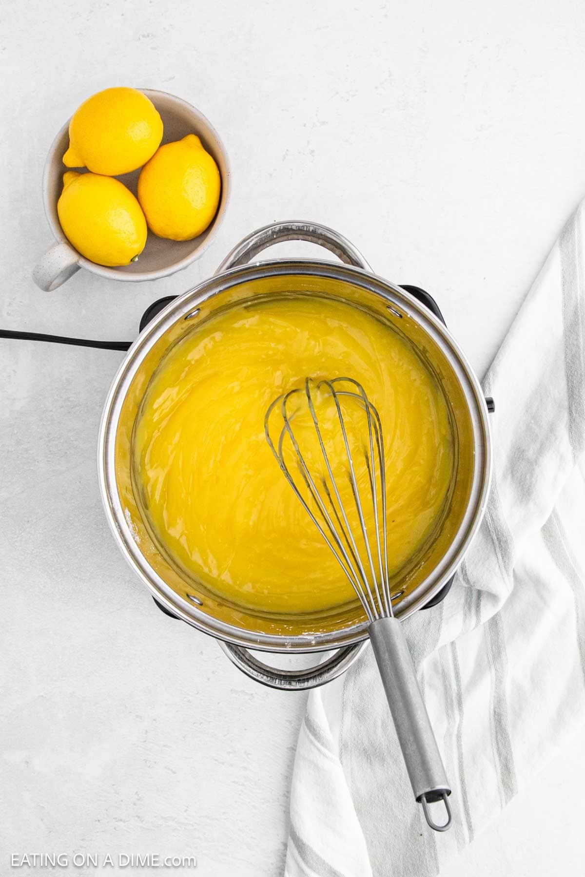 Whisking lemon mixture in a large pot with a small bowl of lemons on the side