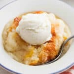 Peach Cobbler in a bowl topped with ice cream.