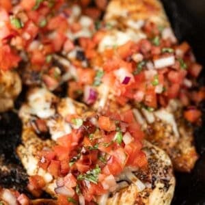 Grilled chicken breasts topped with melted cheese and fresh pico de gallo—diced tomatoes, onions, and cilantro—served in a black skillet. Perfect for adding variety to your Meal Plan 58.