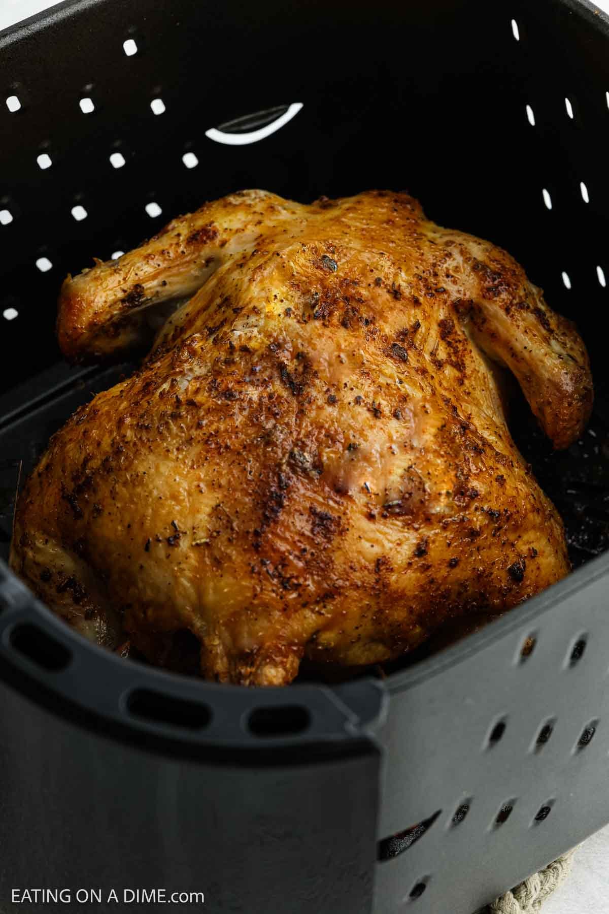 A whole chicken with crispy, golden-brown skin sits inside a black air fryer basket, showcasing one of the best air fryer recipes and ready to be served.