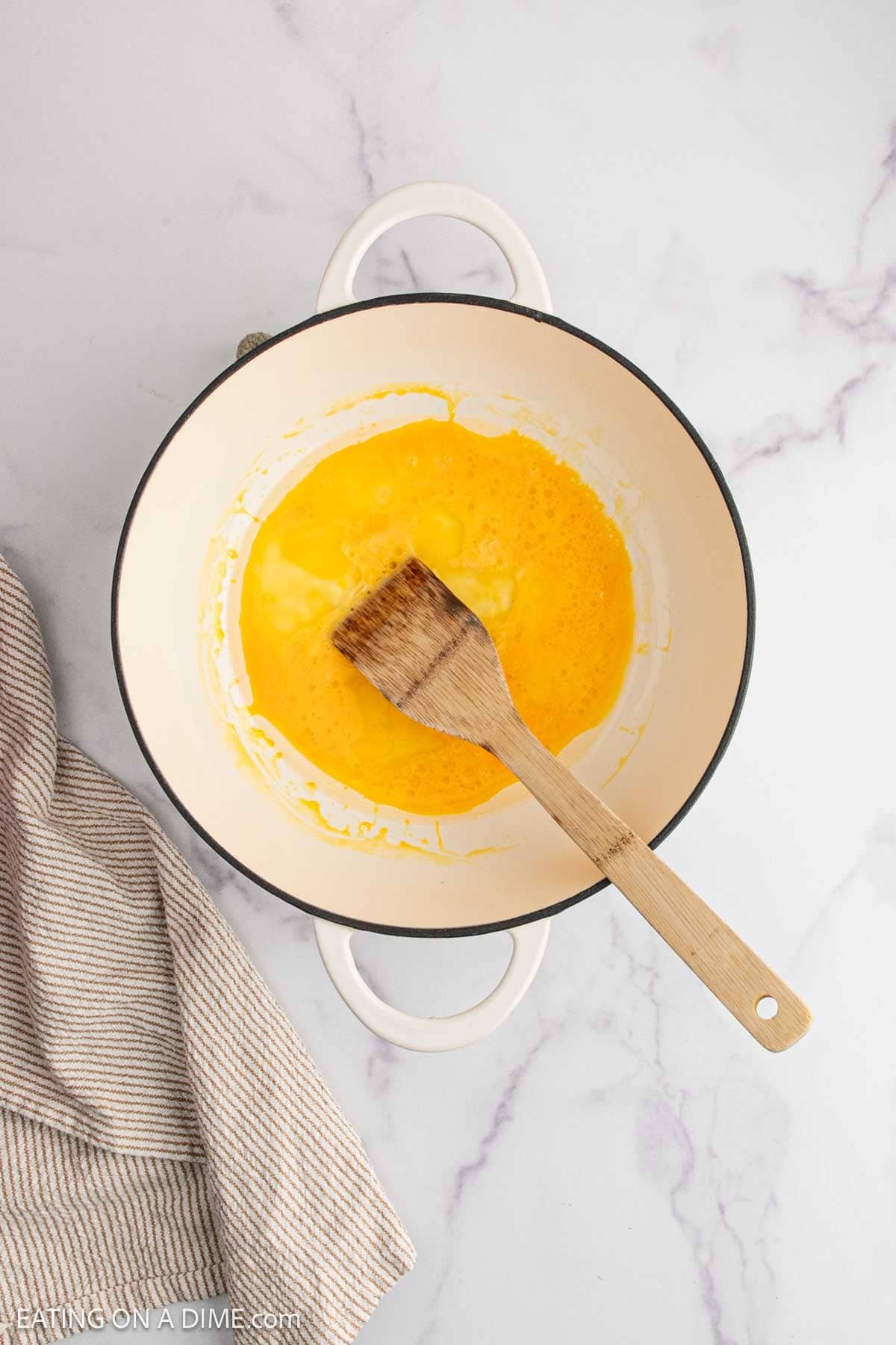 A wooden spatula rests in a white pot with melted butter and flour being stirred together—an essential base for savory dishes like Beef Fried Rice. The pot sits on a marble surface next to a striped kitchen towel.