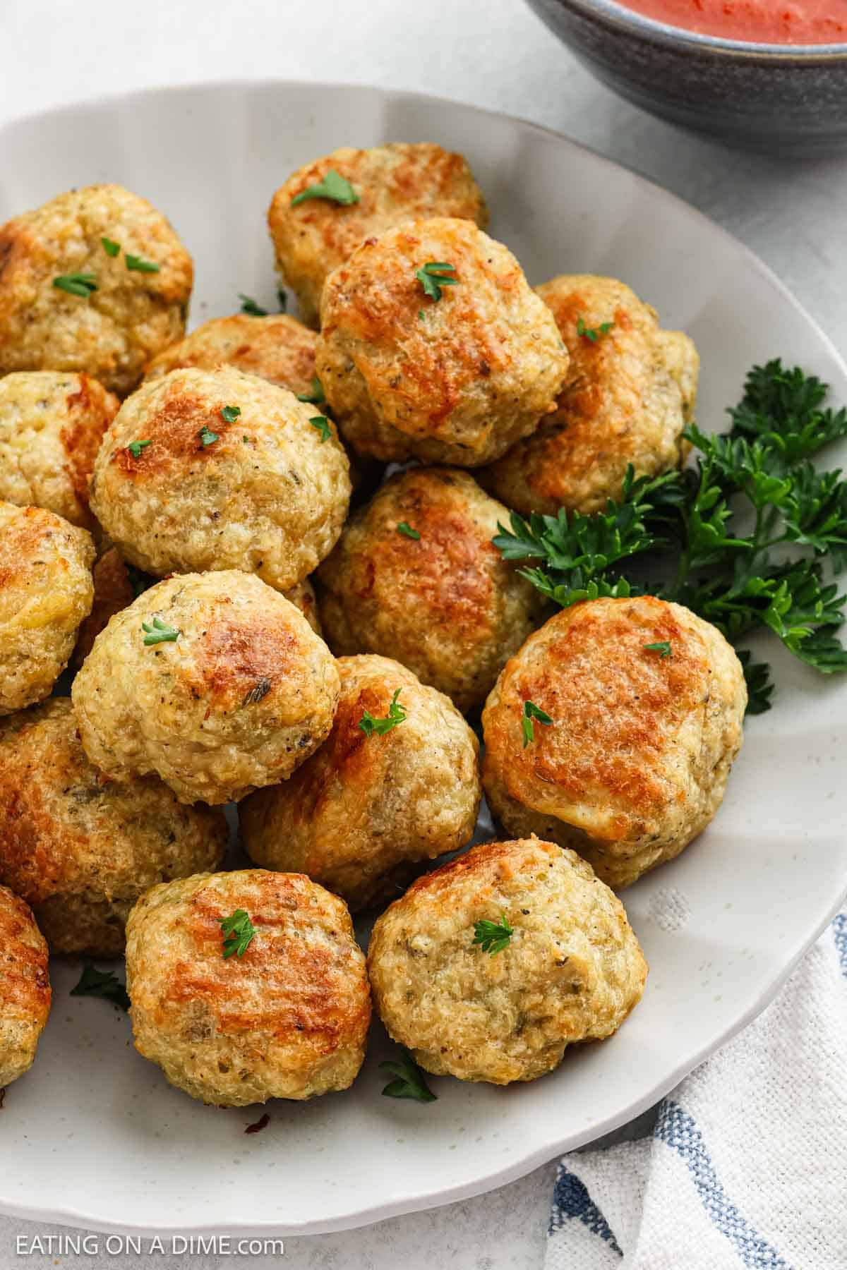 A plate of golden-brown chicken meatballs garnished with fresh parsley, with a bowl of red dipping sauce in the background—perfect for trying a new chicken meatball recipe.