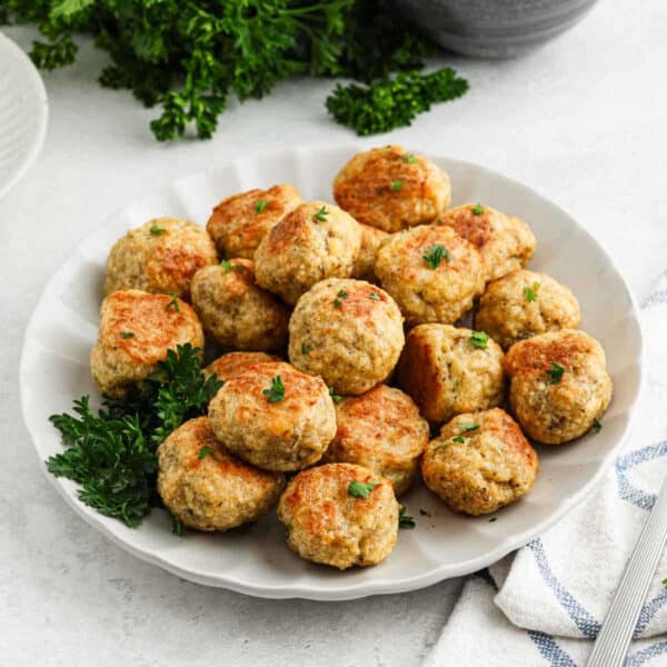 A white plate filled with golden-brown chicken meatballs garnished with fresh parsley, set on a light surface with a sprig of parsley and a striped cloth napkin nearby—perfect for anyone seeking an easy chicken meatball recipe.