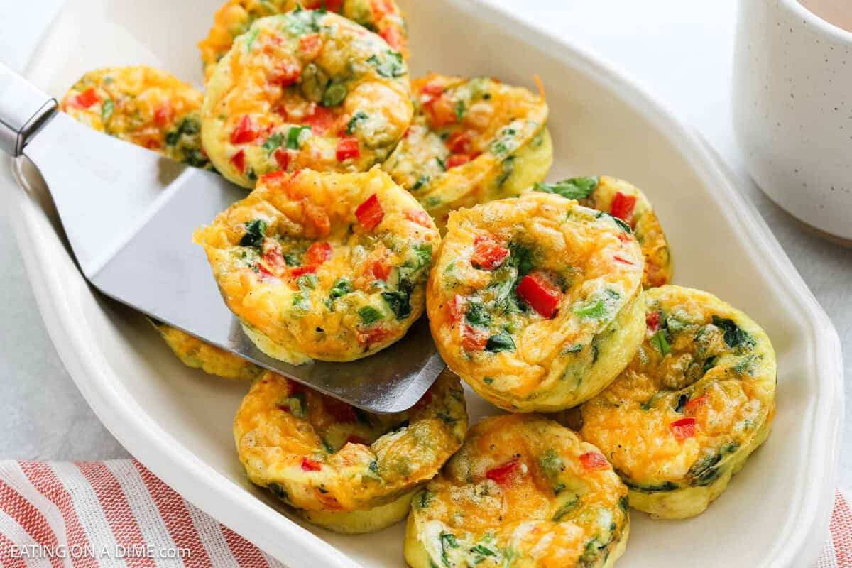 Cottage Cheese Egg Bites stacked on a white platter with a serving spatula.