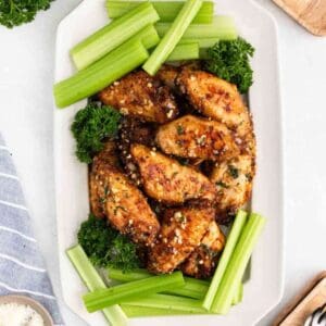 A rectangular white platter with seasoned chicken wings, garnished with parsley and surrounded by fresh celery sticks—perfect for adding to your next Meal Plan 60.