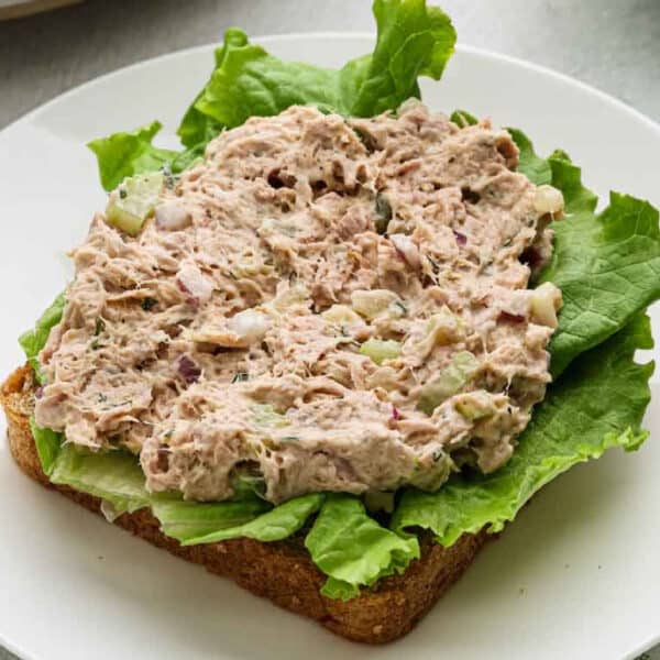 An open-faced tuna salad sandwich with green lettuce on whole wheat bread, served on a white plate.