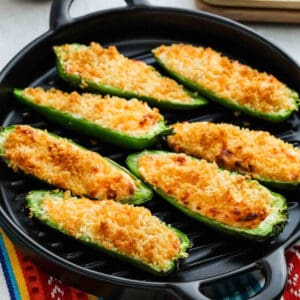 Eight Air Fryer Jalapeño Poppers, stuffed with a creamy, cheesy filling and topped with golden, crispy breadcrumbs, are arranged on a black grill pan.