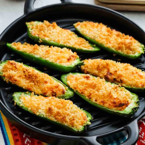Eight Air Fryer Jalapeño Poppers, stuffed with a creamy, cheesy filling and topped with golden, crispy breadcrumbs, are arranged on a black grill pan.