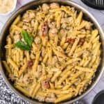 A skillet filled with creamy Chicken Pesto Pasta, tender chicken pieces, sun-dried tomatoes, and garnished with fresh basil leaves.