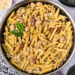A skillet filled with creamy Chicken Pesto Pasta, tender chicken pieces, sun-dried tomatoes, and garnished with fresh basil leaves.
