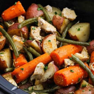 A close-up of Slow Cooker Chicken and Vegetables, featuring tender chicken pieces, green beans, carrots, and red potatoes seasoned with herbs and black pepper.