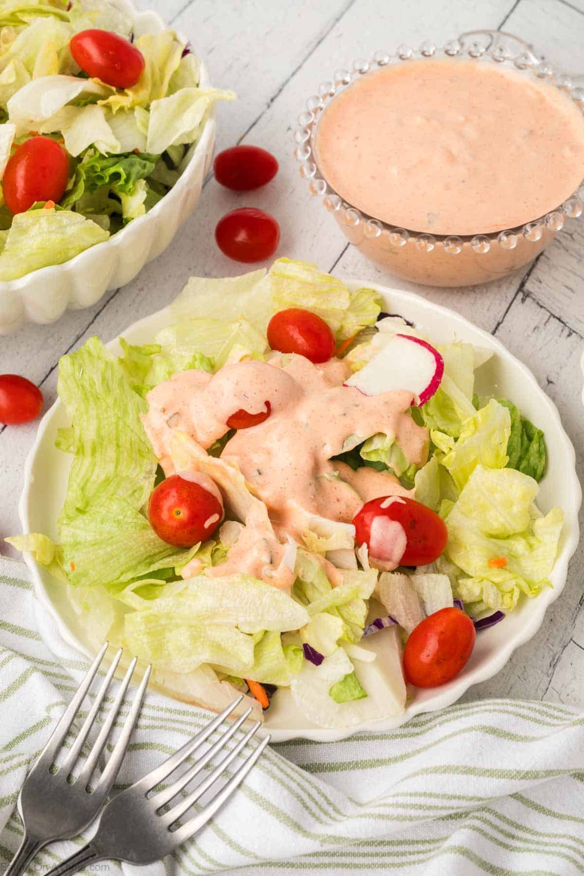 Thousand Island Dressing drizzled over salad with cherry tomatoes on a plate with a bowl of Thousand Island Dressing on the side